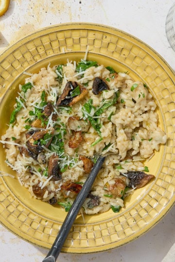 a uellow bowl of risotto with lemons and a napkin on the side