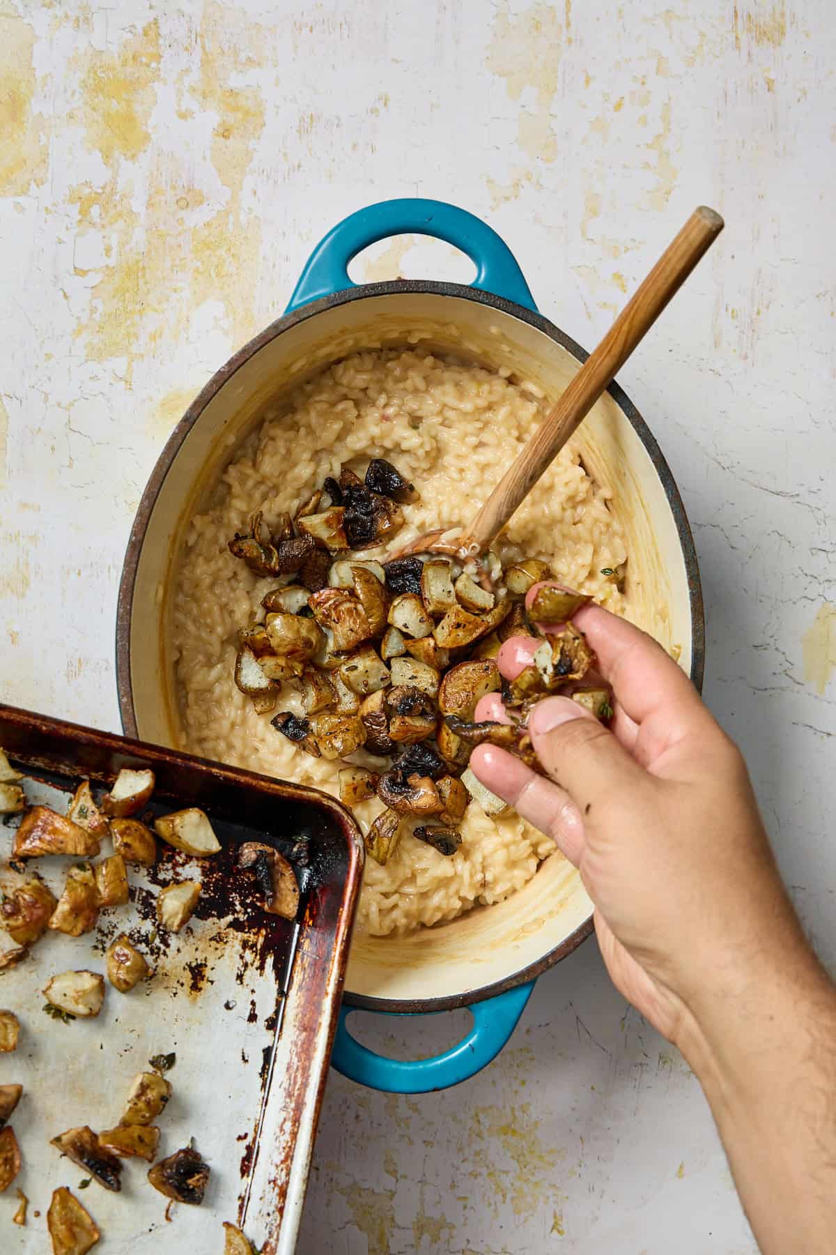 roasted mushrooms and jerusalem artichokes being added by hand into the pot of risotto