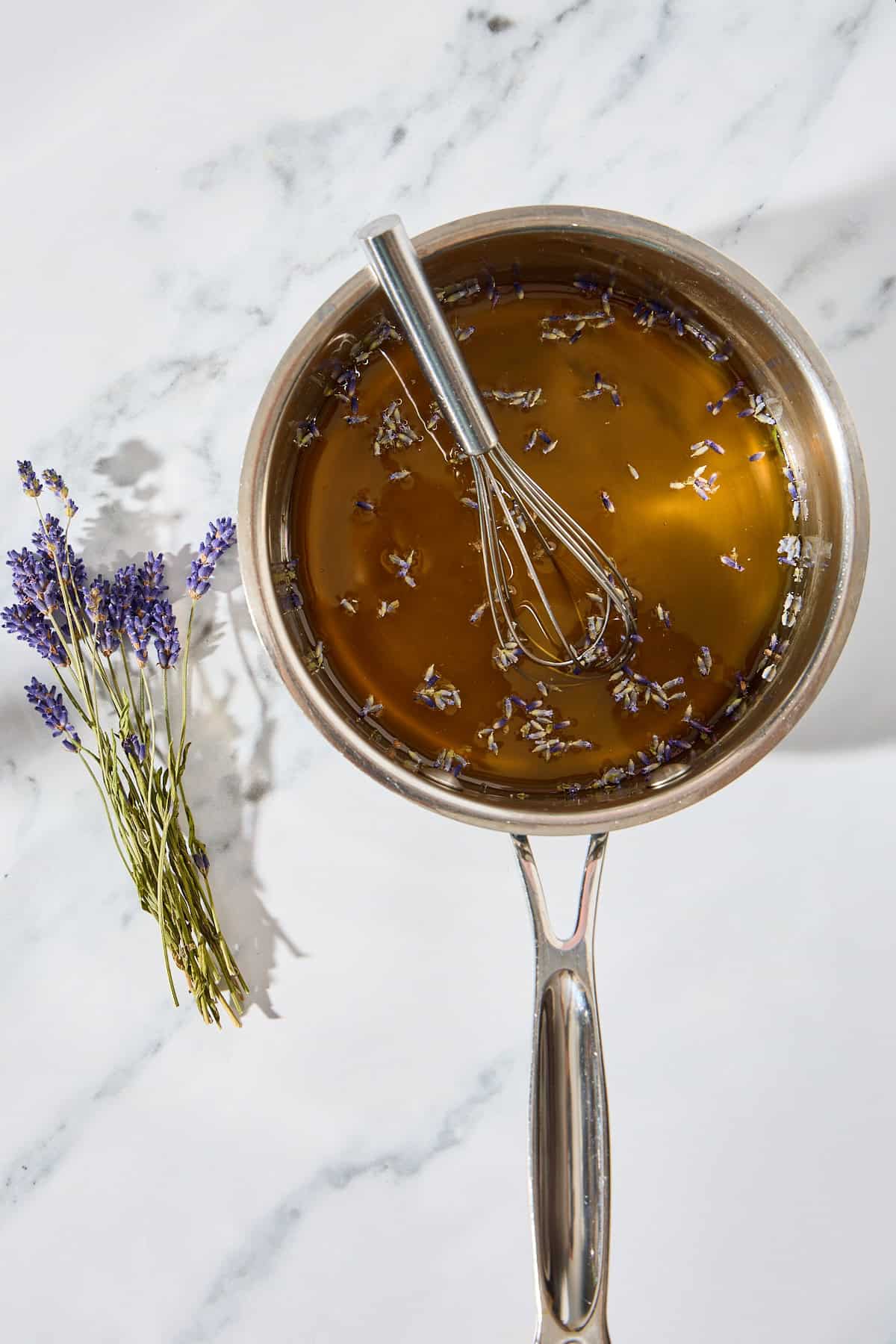 a small pot with simple syrup with a whisk and lavender buds