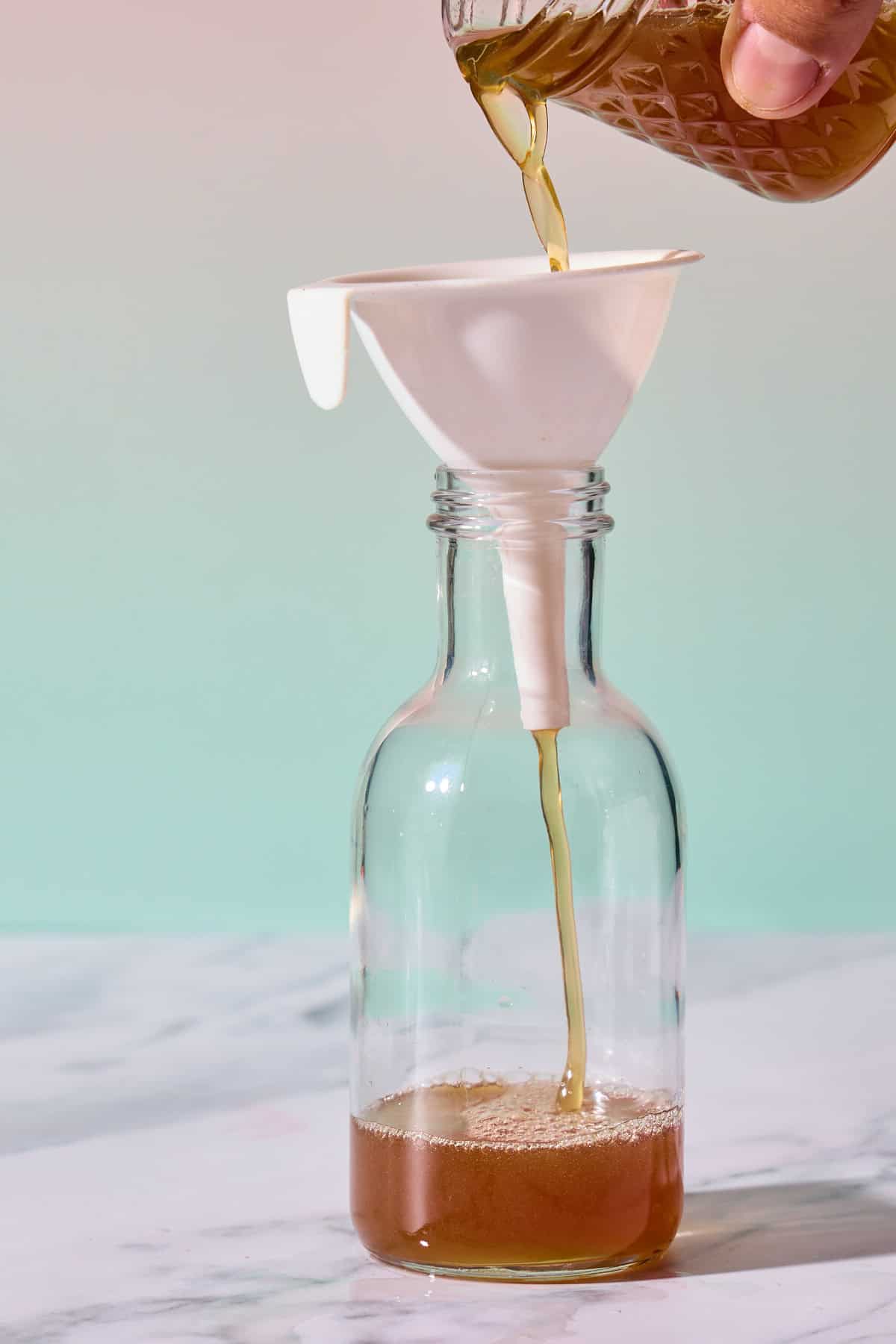 simple syrup being poured through a funnel into a small bottle