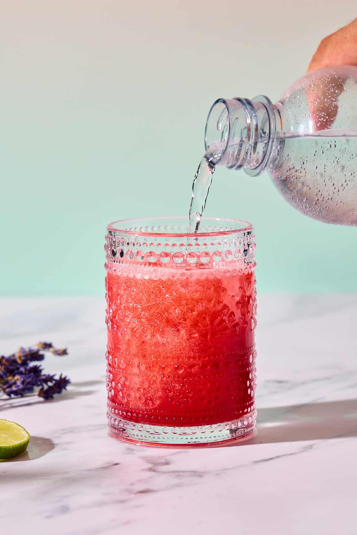 bottle of club soda being poured into raspberry mocktail glass