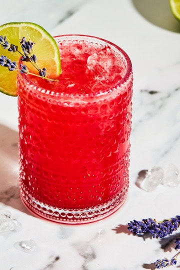 a glass filled with a red mocktail and ice with limes and lavender