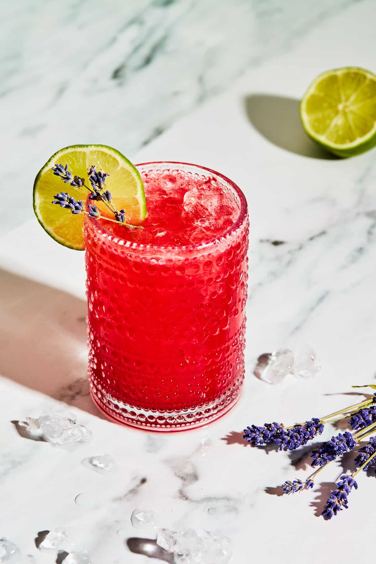 a glass filled with a red mocktail with a lime slice and lavender garnish