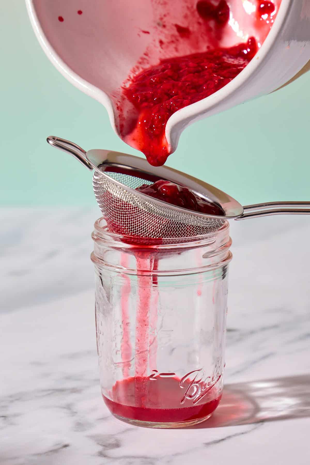 raspberry puree being poured through a strainer into a jar