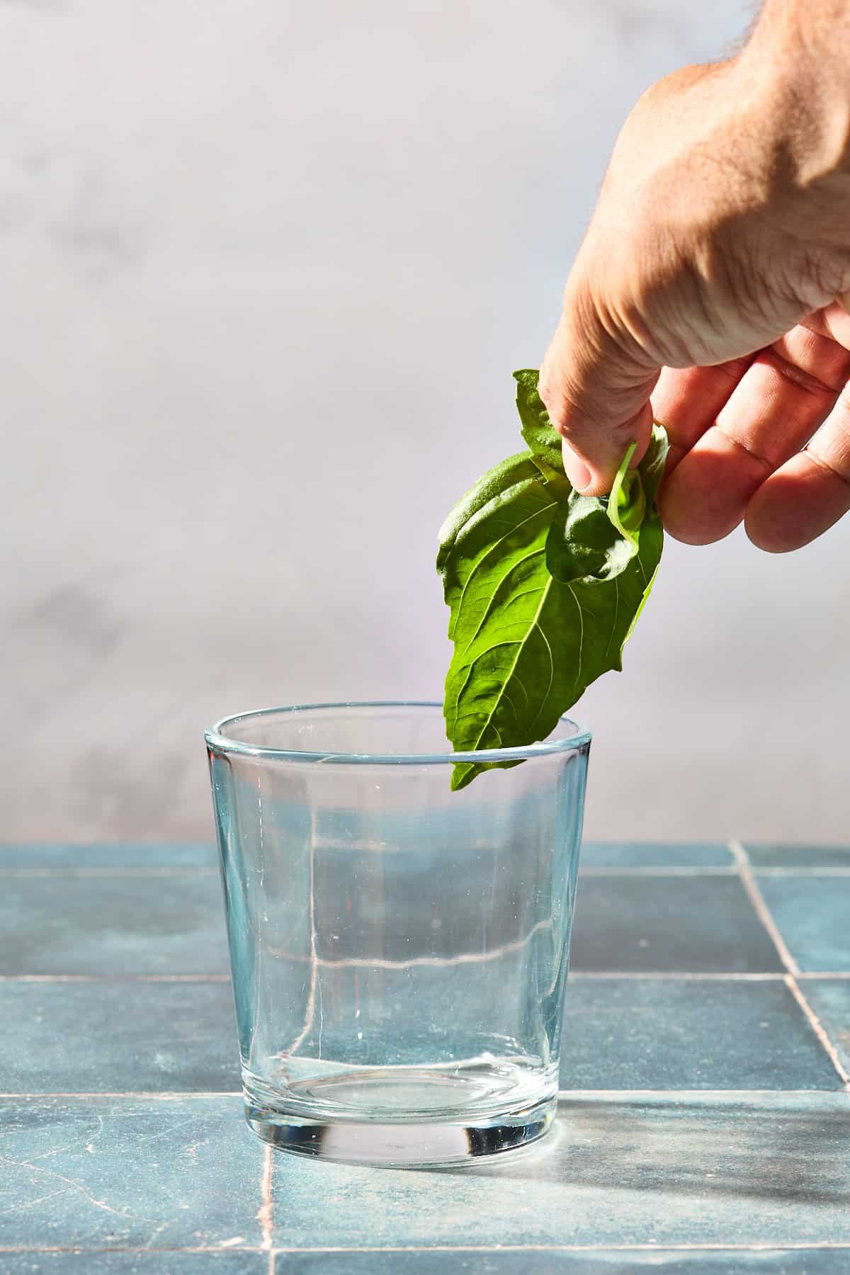 a piece of basil being dropped into a glass on a blue counter