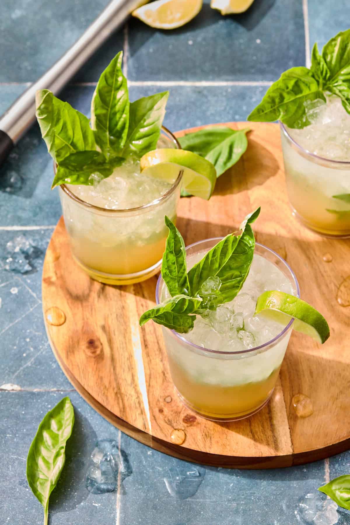 glasses of mojotios with basil and lime and ice on a wooden board set on a blue tiled counter