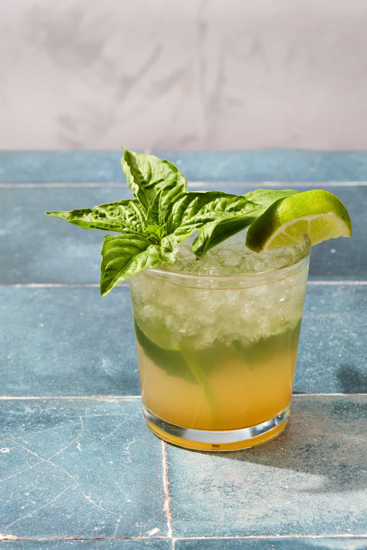 a mojito on a blue tiled counter that is garnished with basil and lime