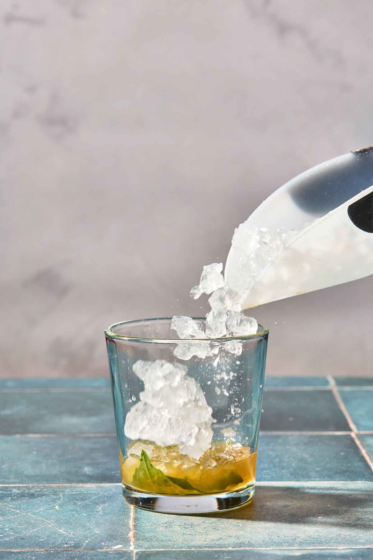 ice being poured into a cocktail glass with basil