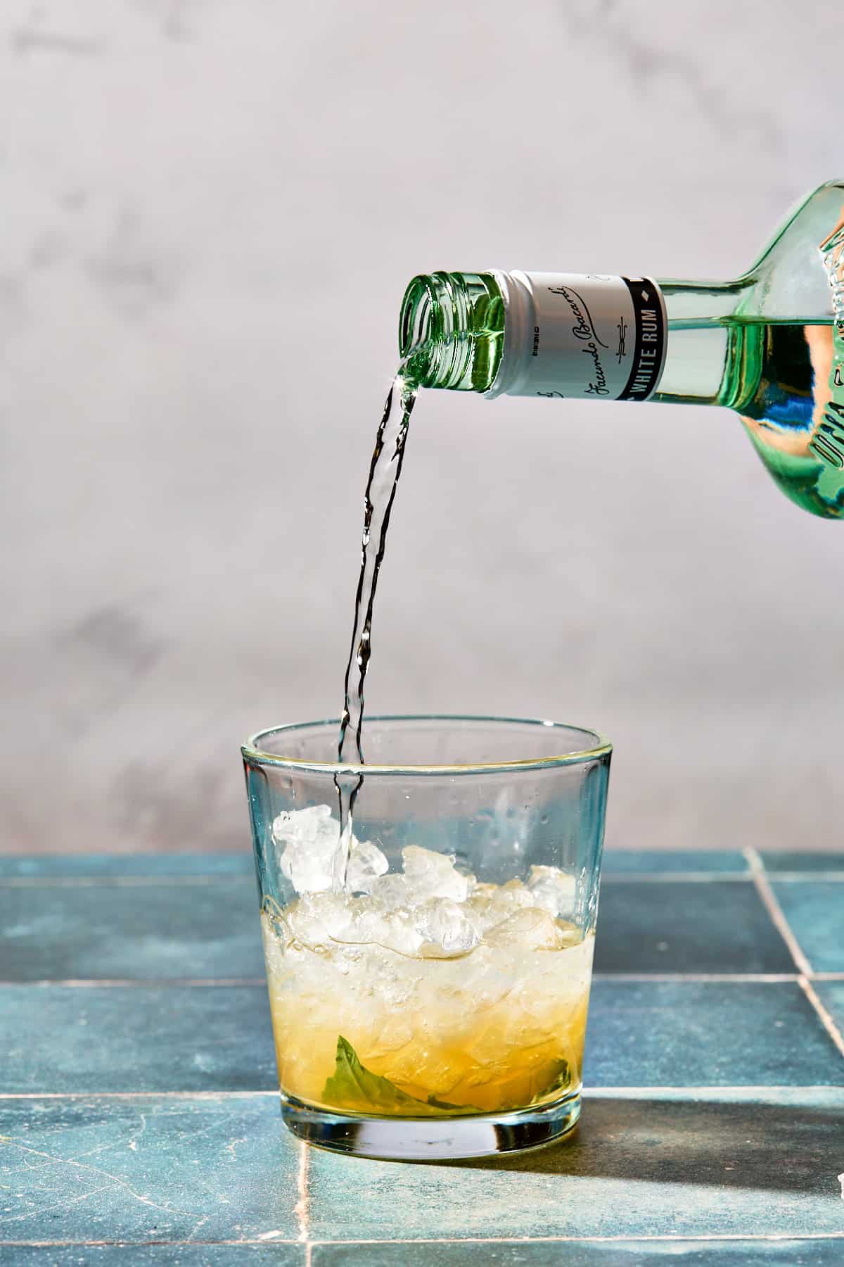 a bottle of white rum being poured into the cocktail glass with ice