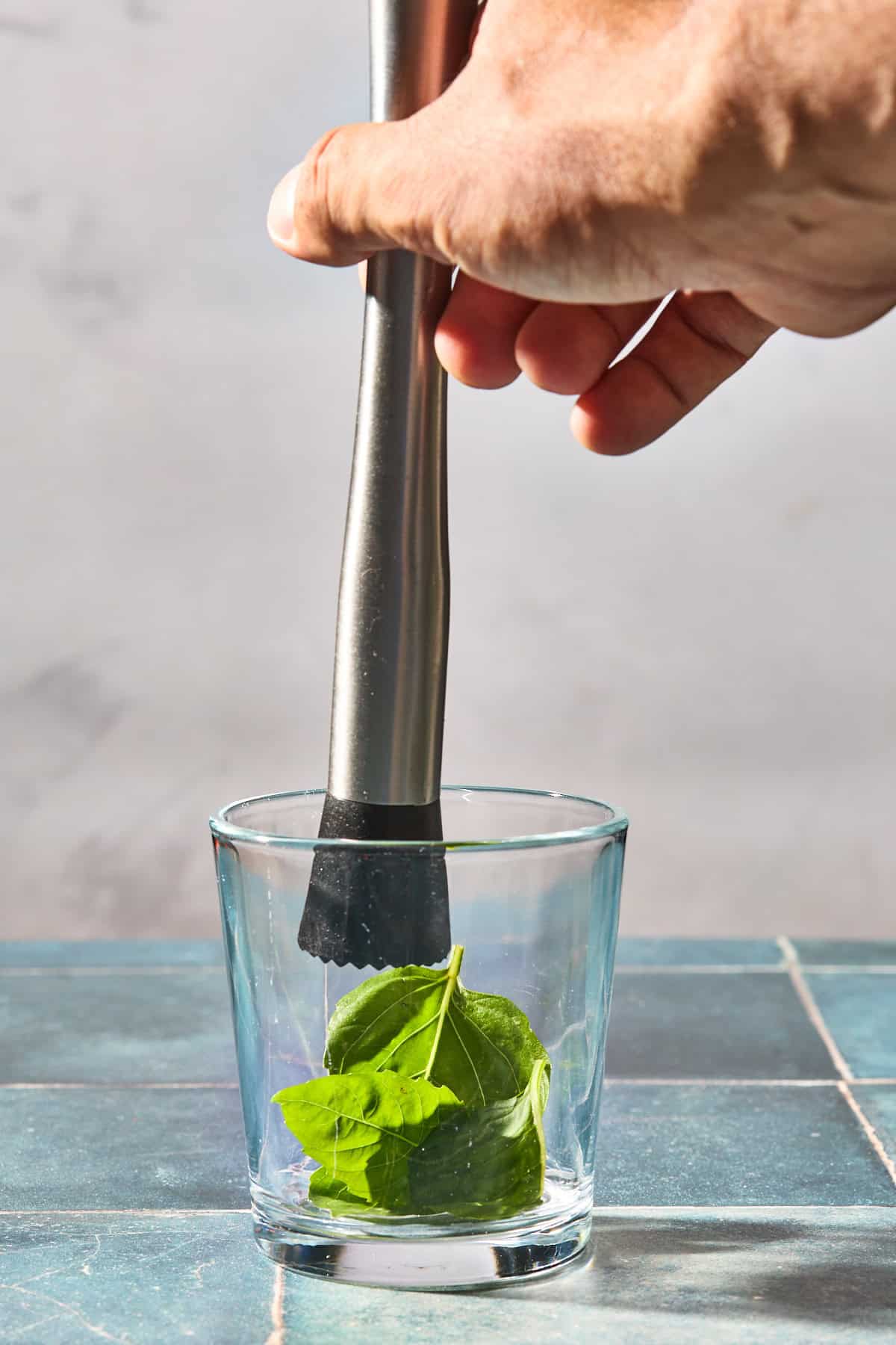 a piece of basil being muddled in a glass on a blue counter
