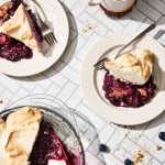 plates of blueberry pie topped with meringue and a pie dish with blueberries on a white counter