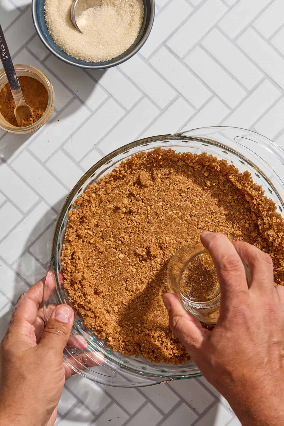 graham crackers being pressed into a pie plate with a glass