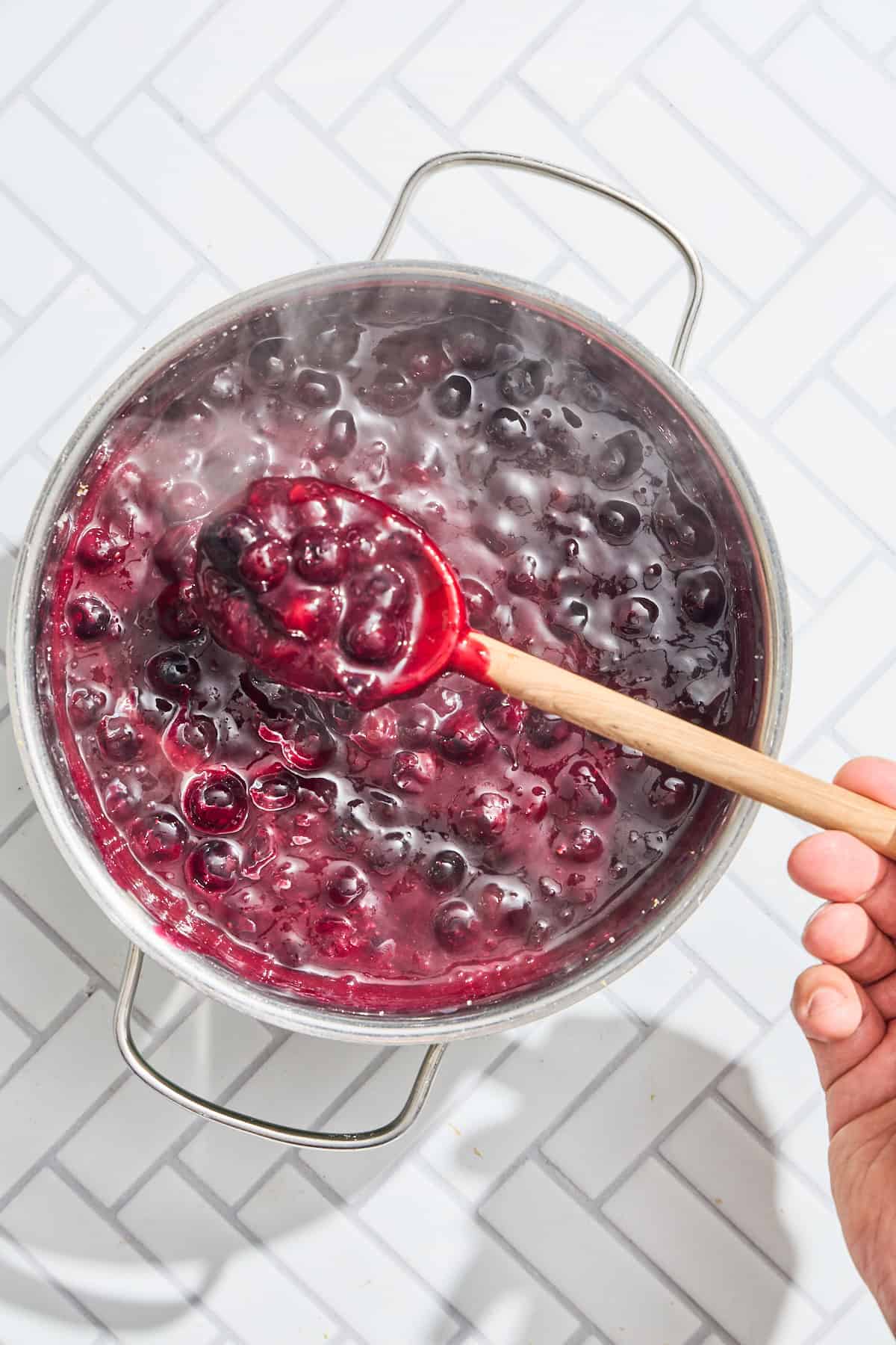 a pot of blueberry pie filling with a woden spoon scooping some out of the pan
