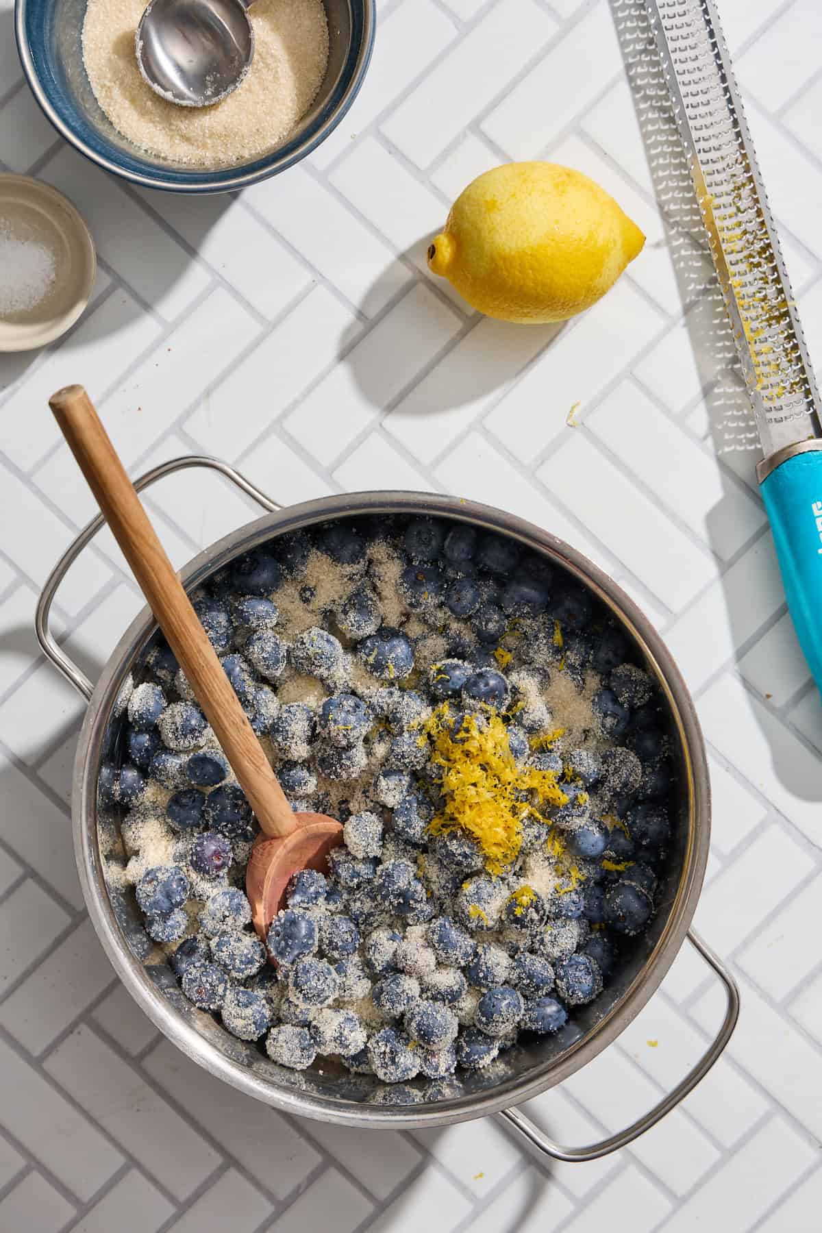 a pot of blueberries with lemon zest and a wooden spoon