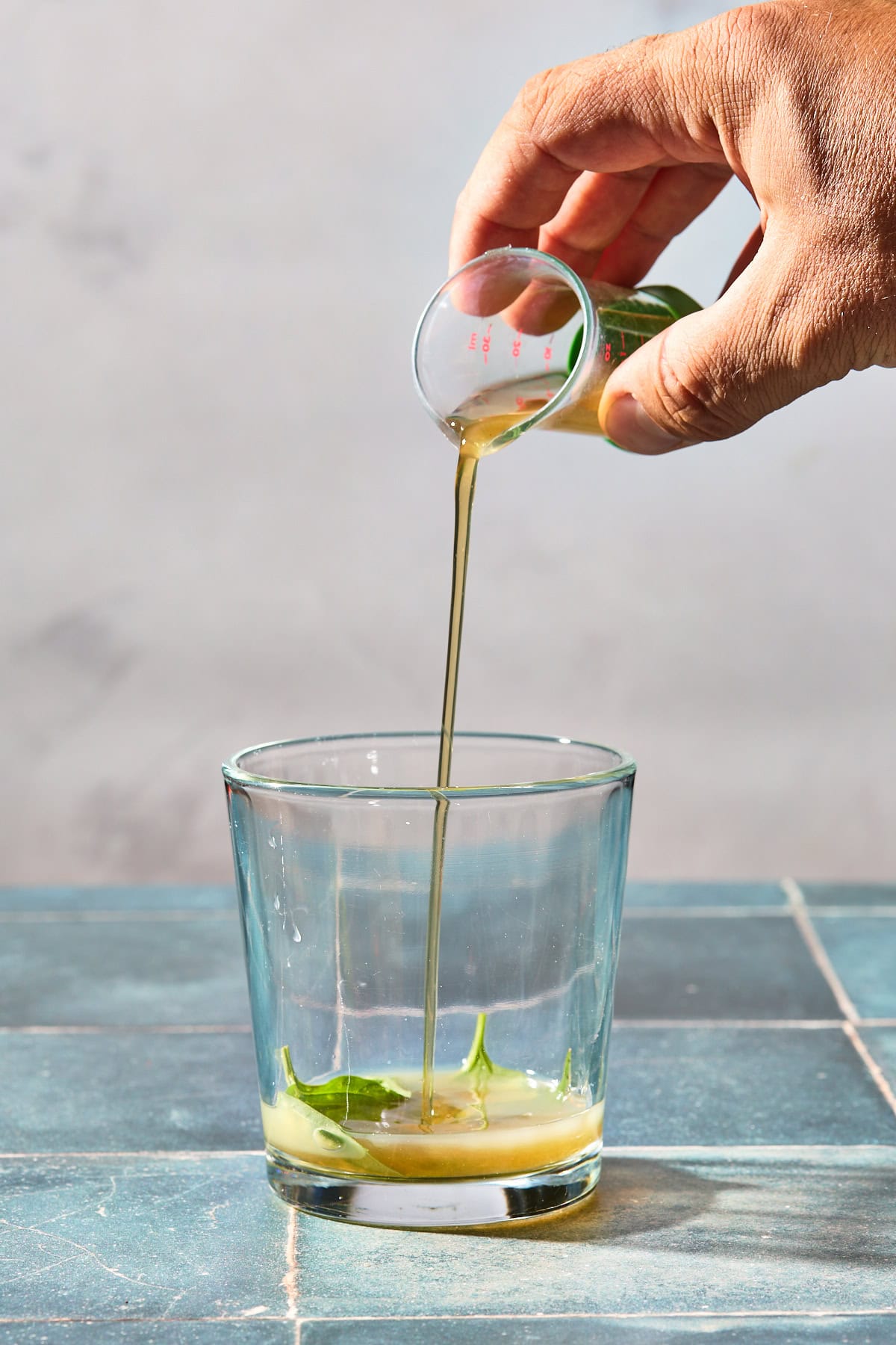 simple syrup being poured into a glass with basil and lime juice