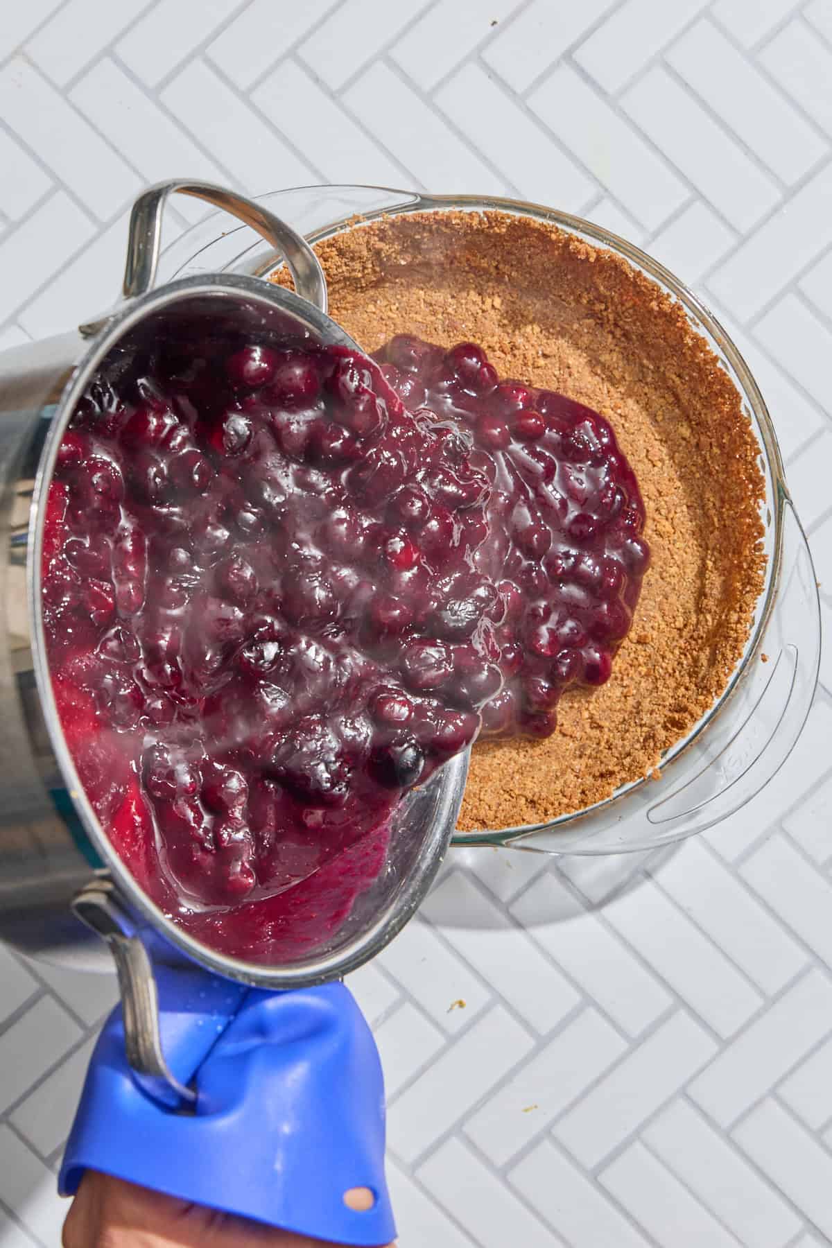 blueberry pie filling being poured into graham cracker pie crust