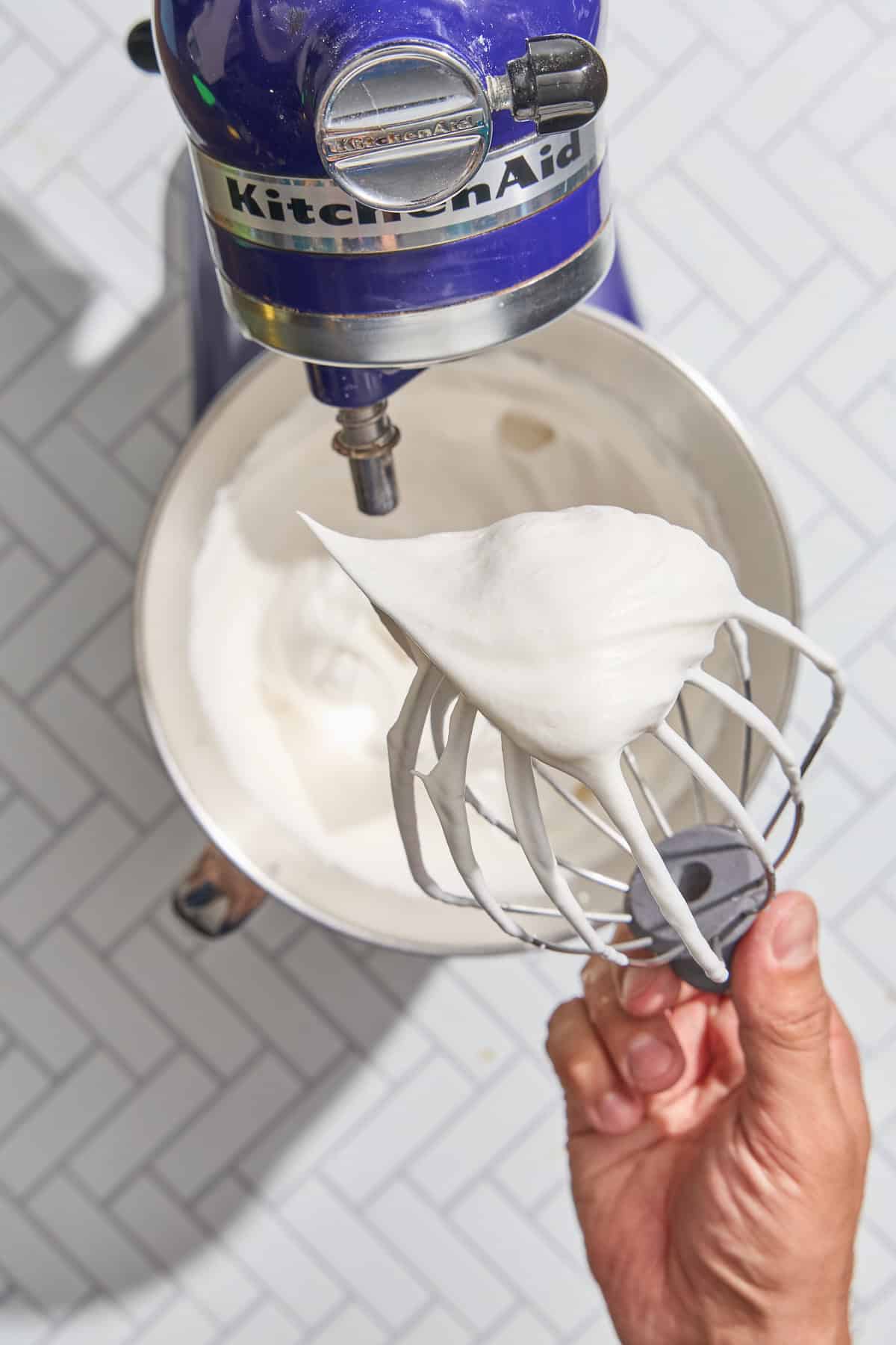 meringue on a mixer beater over a bowl of whipped meringue