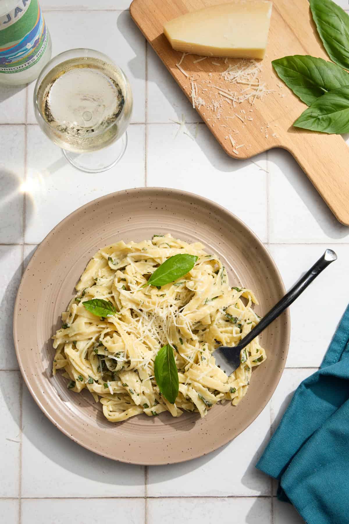 a palte of alfredo pasta with cheese, wine and basil