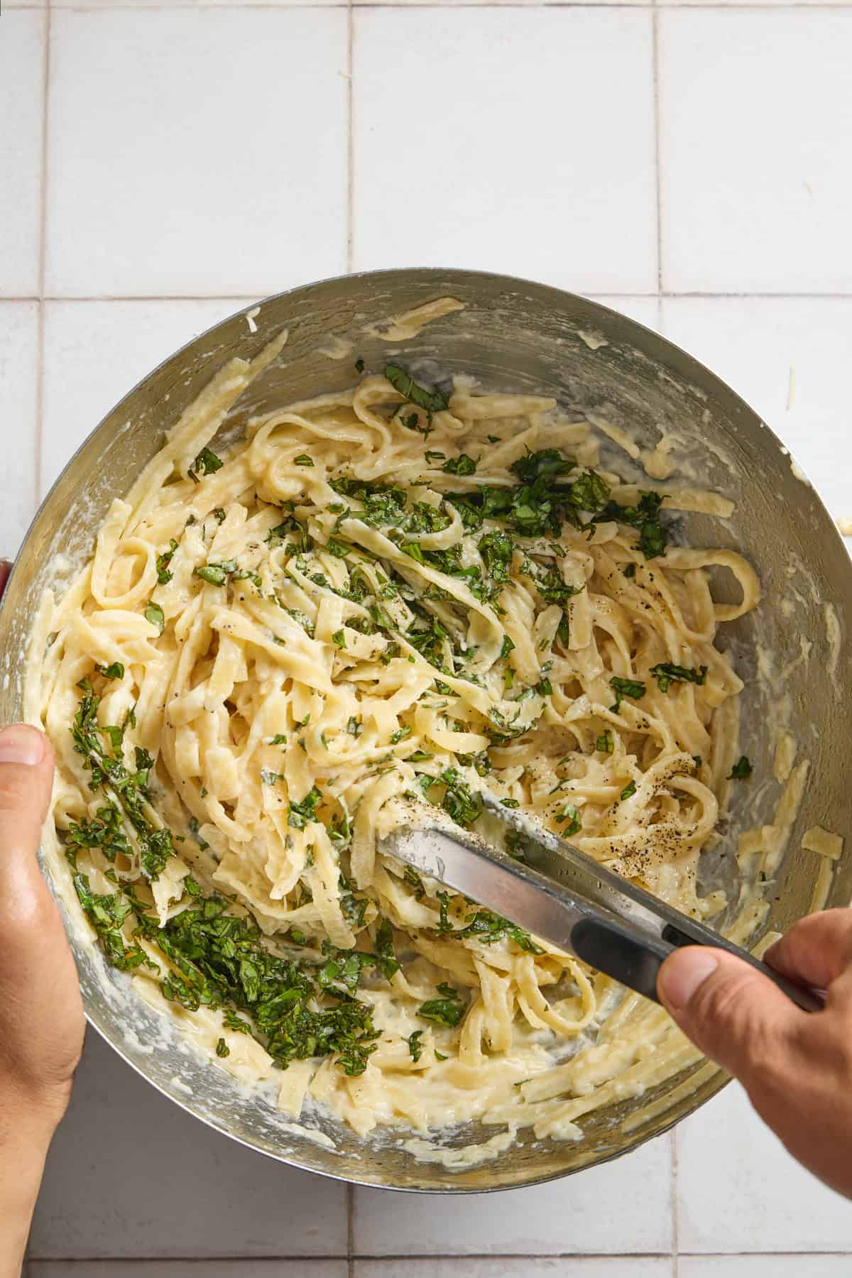 chopped basil being stirred into a bowl of alfredo pasta