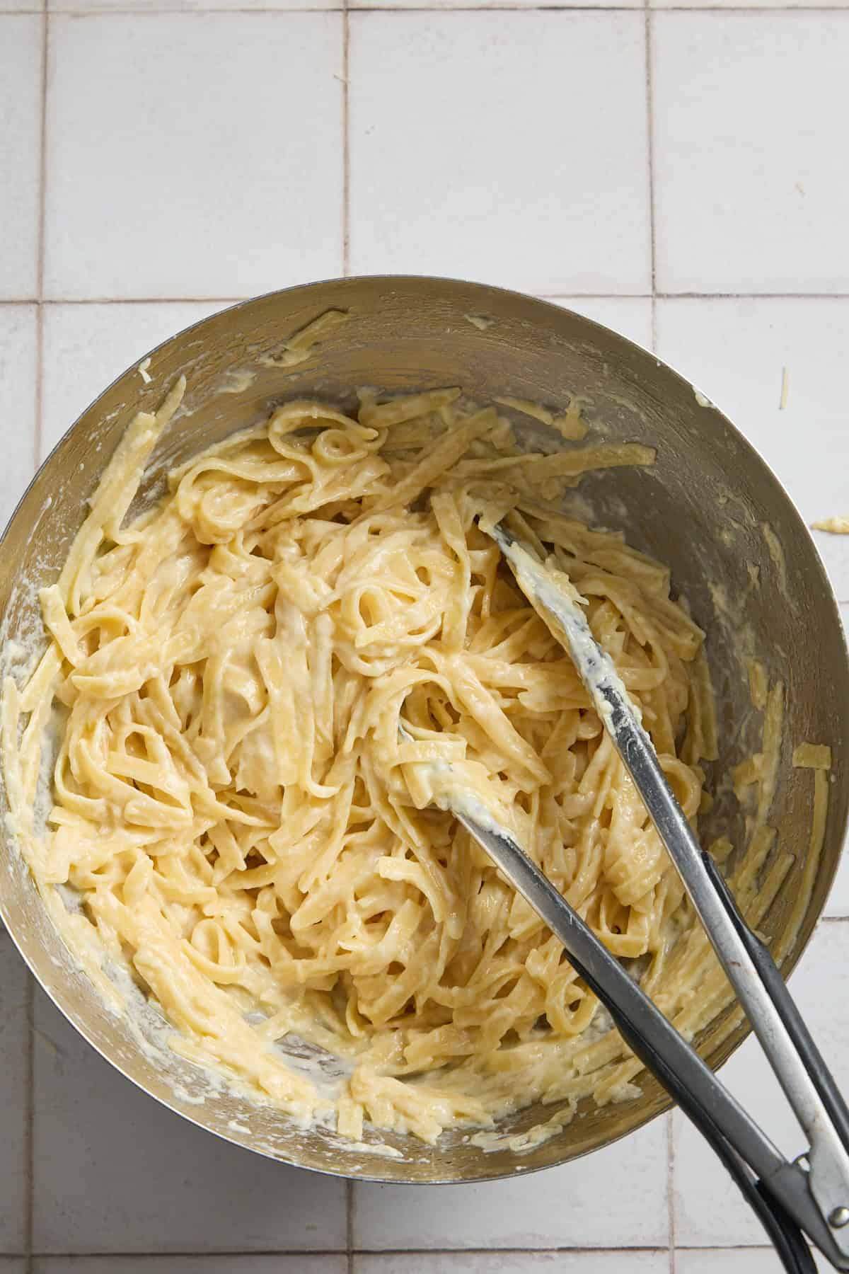 alfredo sauce being mixed on fettucine in a large bowl