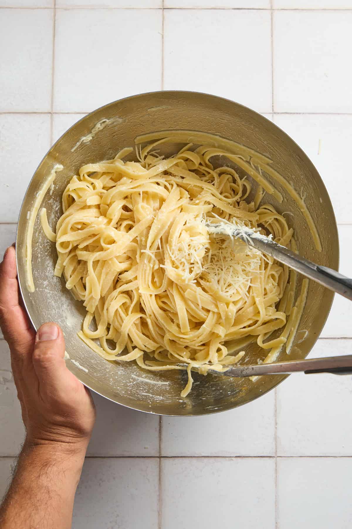 shredded parmesan cheese being tossed in bowl with pasta