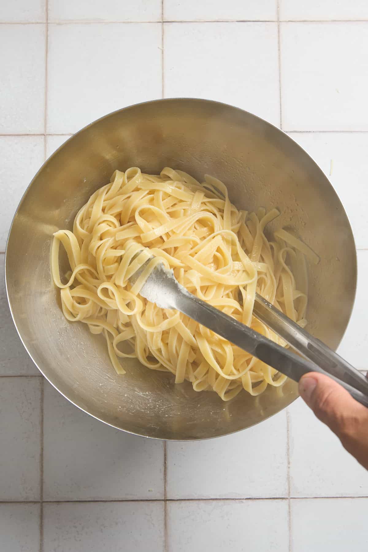 fettucine being added to a bowl of butter with tongs