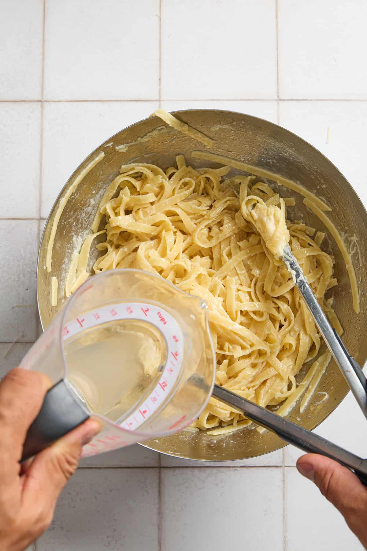 pasta water being poured into a bowl of cooked pasta and cheese